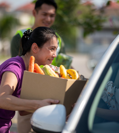 Asian female food bank volunteer received donation food at a drive through food bank.