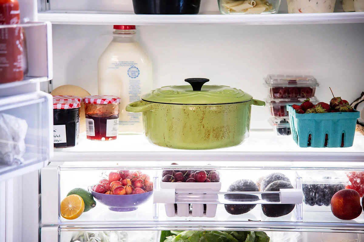 Inside a refrigerator with a variety of produce, milk, and a dutch oven
