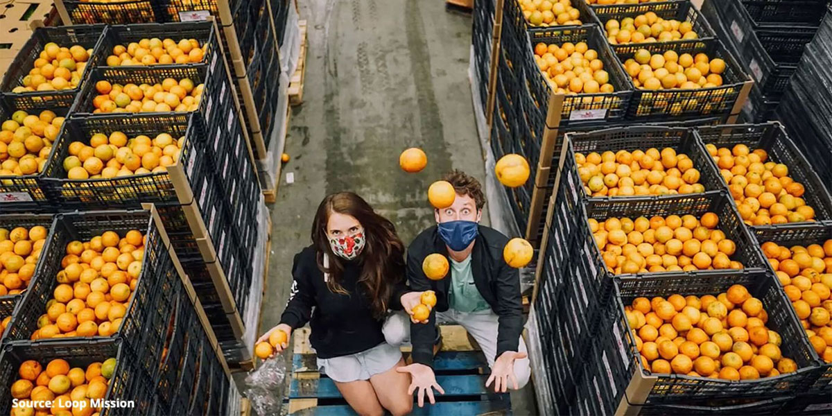 Two people wearing face masks standing among cases of oranges