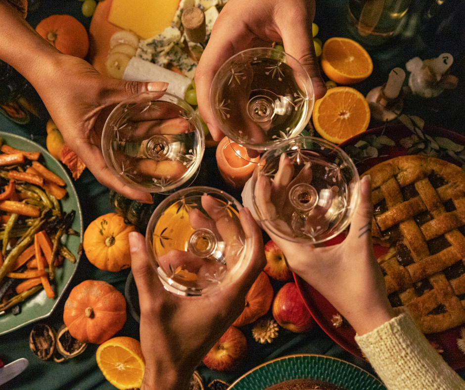 friends cheers with dainty cocktail glasses over an abundant thanksgiving meal